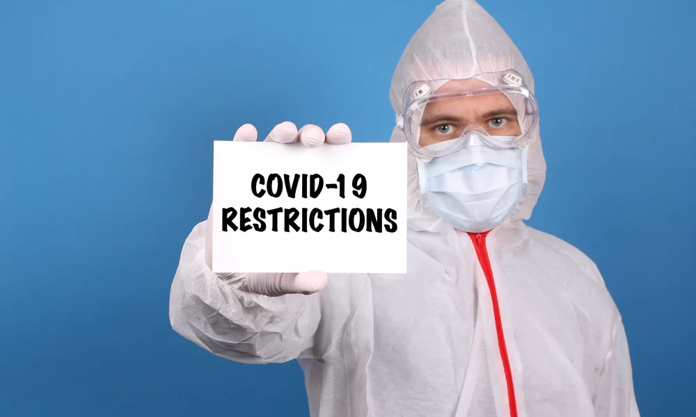 Medical doctor holding banner with Covid-19 Restrictions text, Isolated over blue background