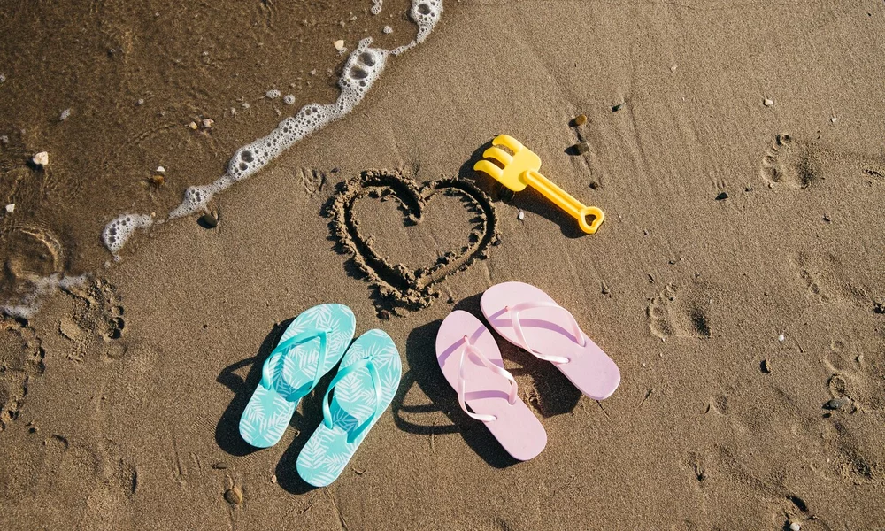 A couple's flipflops laying on the beach with a love heart drawn in the sand