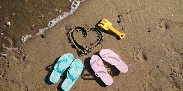 A couple's flipflops laying on the beach with a love heart drawn in the sand
