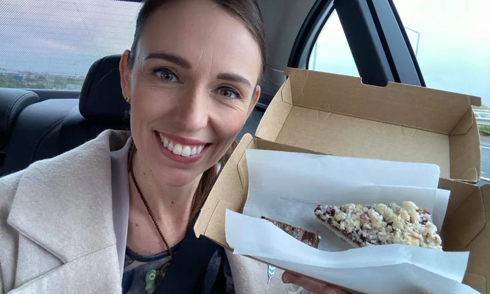 Jacinda Ardern smiling in the camera, posing with a piece of pie.