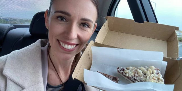 Jacinda Ardern smiling in the camera, posing with a piece of pie.