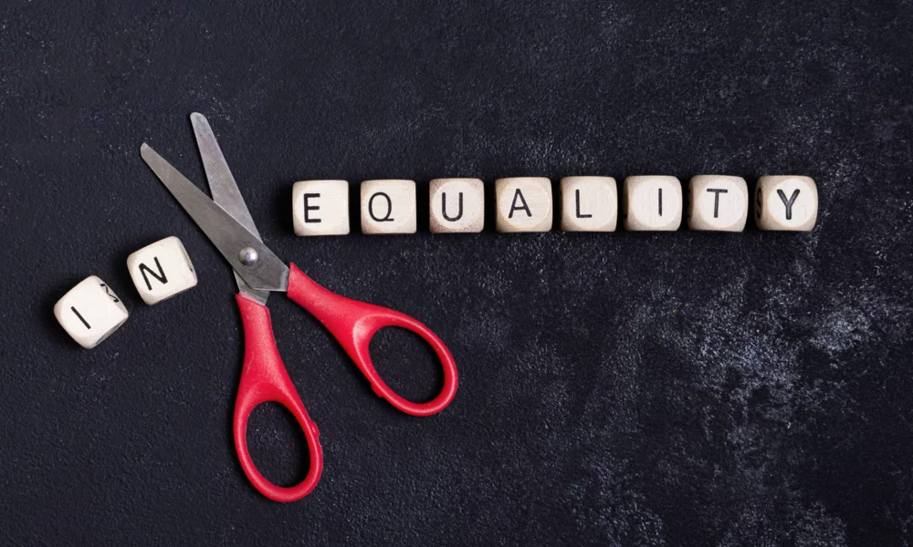 black background with scrabble letters that spell the work inequality. between in and equality there is a scissor.
