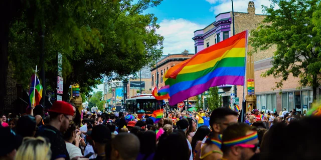A big crowd at a pride parade, with a rainbow flag in the middle